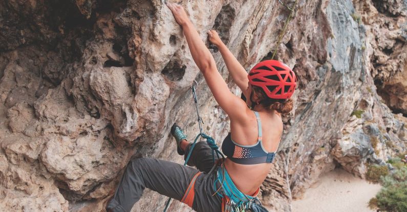 Safety Practices - Side view of anonymous female with rope in helmet climbing on stony terrain